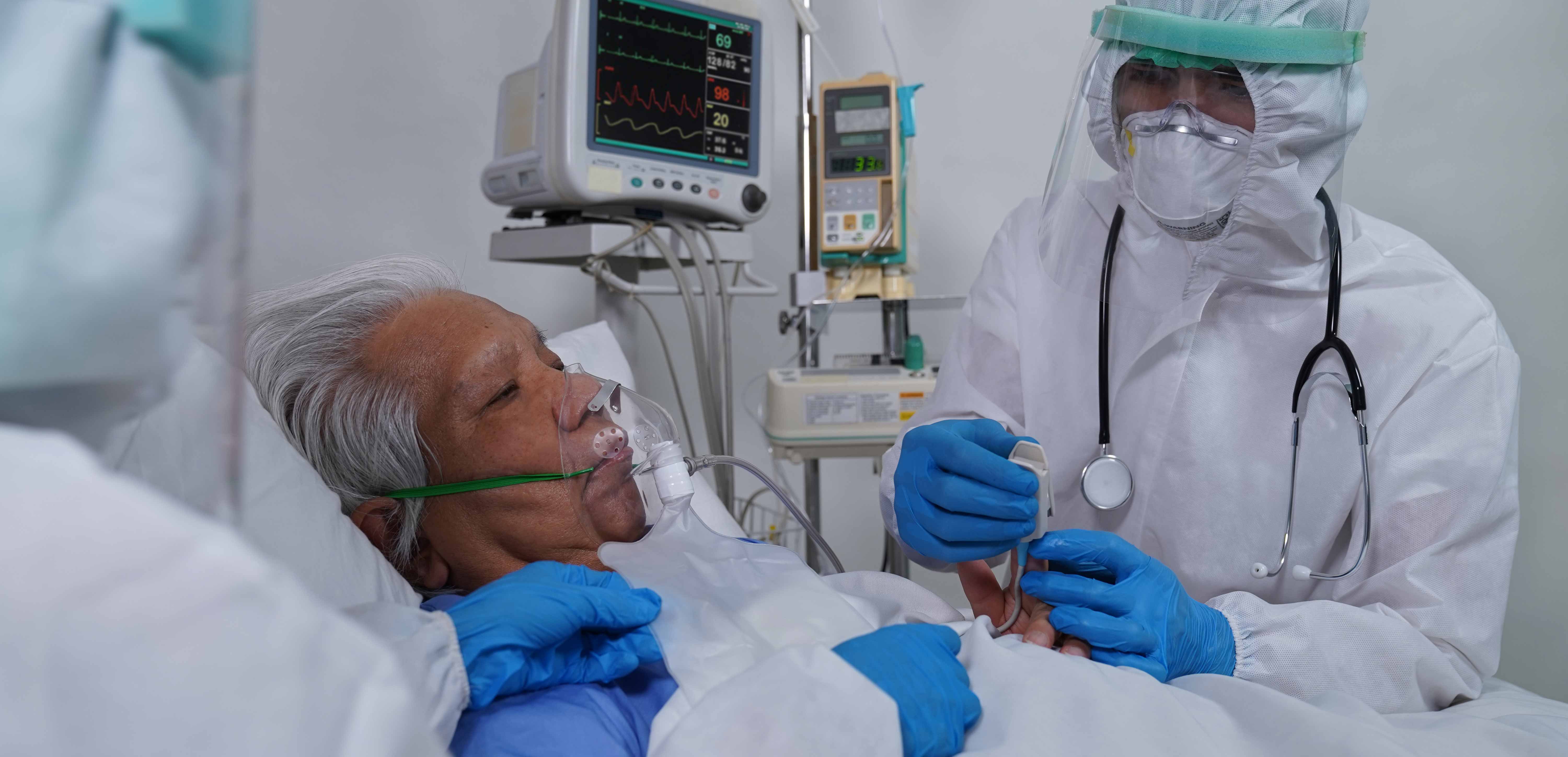 Imagem de dois médicos com equipamentos de proteção individual contra o COVID cuidando de um paciente idoso